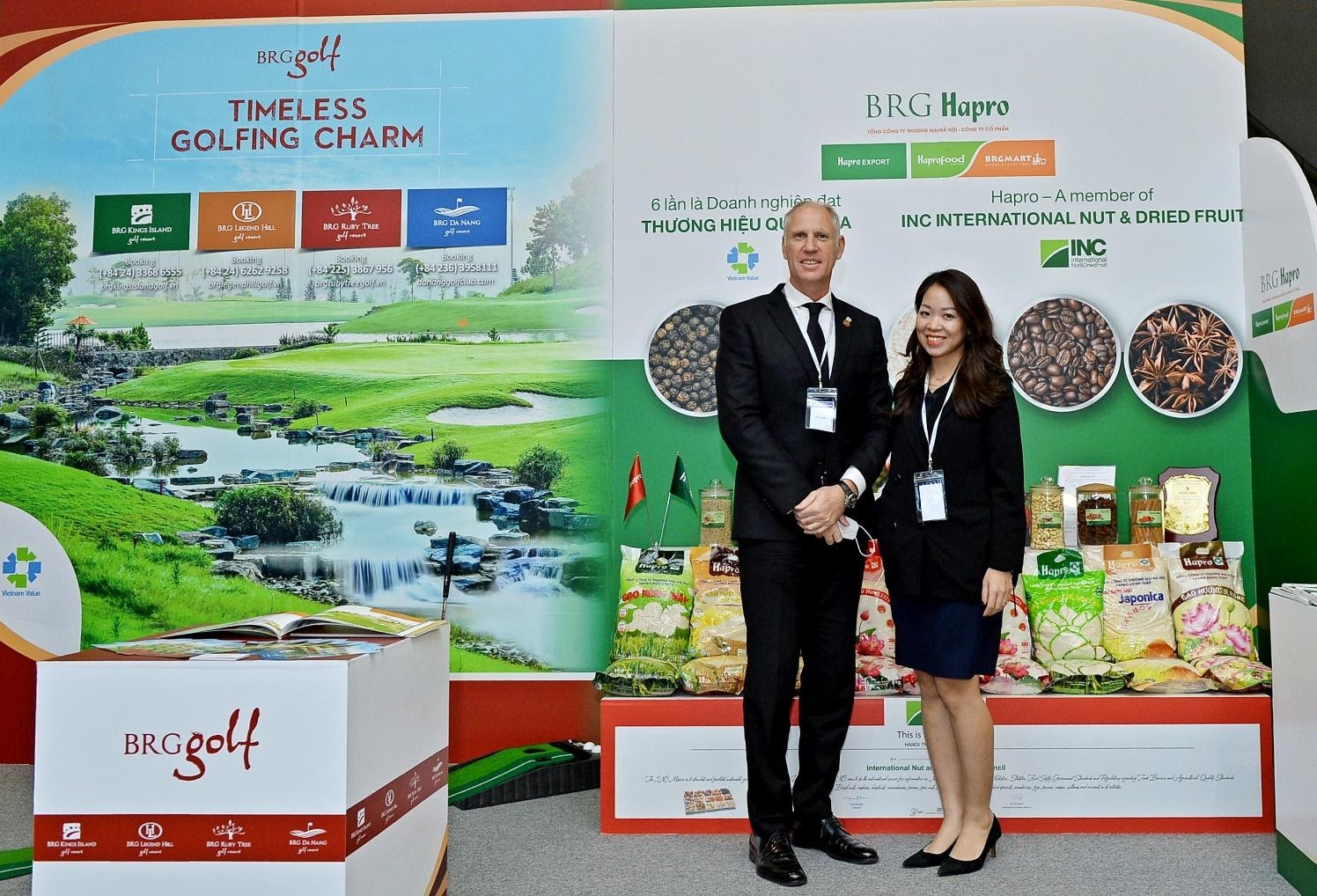 Two people standing next to each other in front of a displayDescription automatically generated with medium confidence